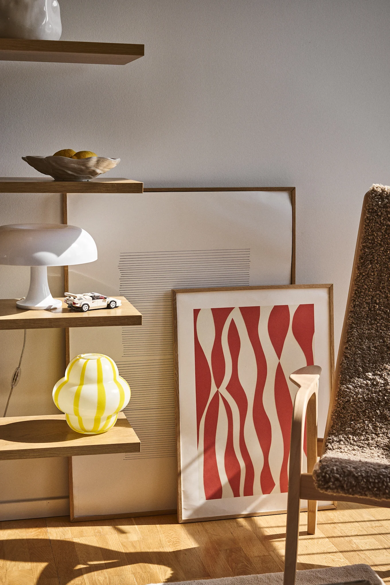 En hylla med en lekfull gul vas, placerad bredvid tavlor som lutar mot golvet och en fotölj – en oväntad och färgstark inredning som följer inredningstrenderna för 2026.