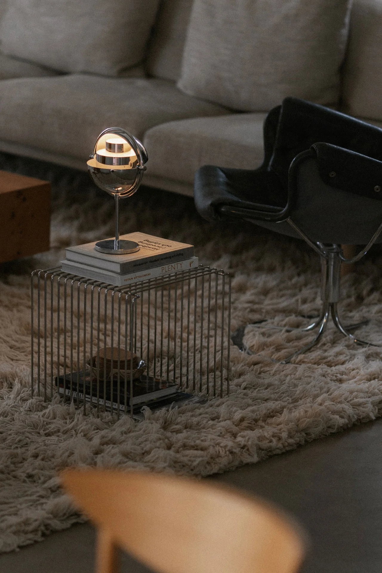 En mässingsbordslampa med en tänd vit kupolformad skärm står på en fönsterbräda bredvid en vit vas med grenar, med utsikt utomhus.