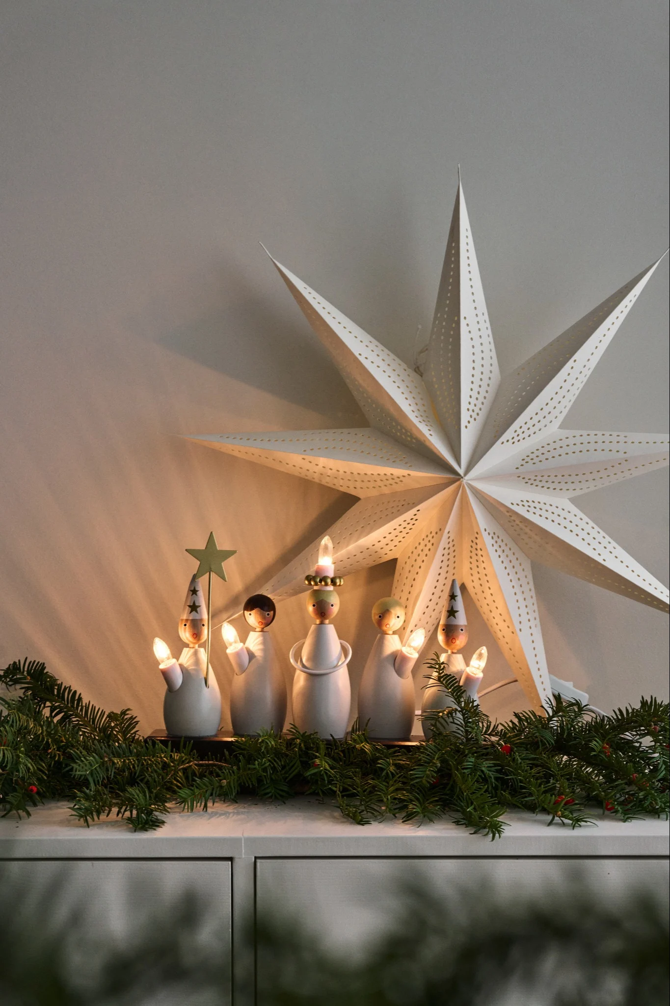 En adventslljustake med ett luciatåg står och lyser på en byrå dekorerat tillsammans med granris.