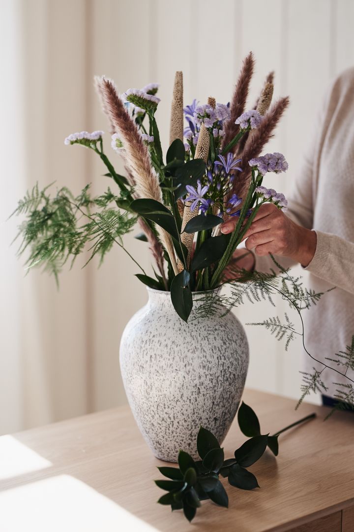 Vit, hög vas i keramik från Knabstrup Keramik står på bordet med snittblommor ifrån Blombruket. 
