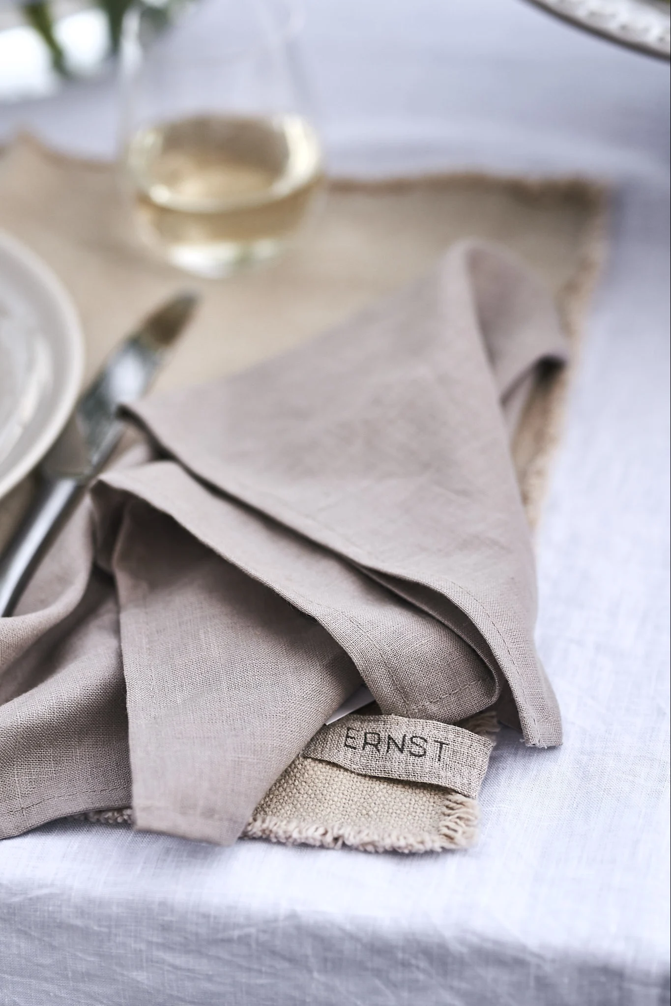 Naturfärgad linneservett ligger ledigt vikt på bordet ovanpå en bordstablett från ERNST.