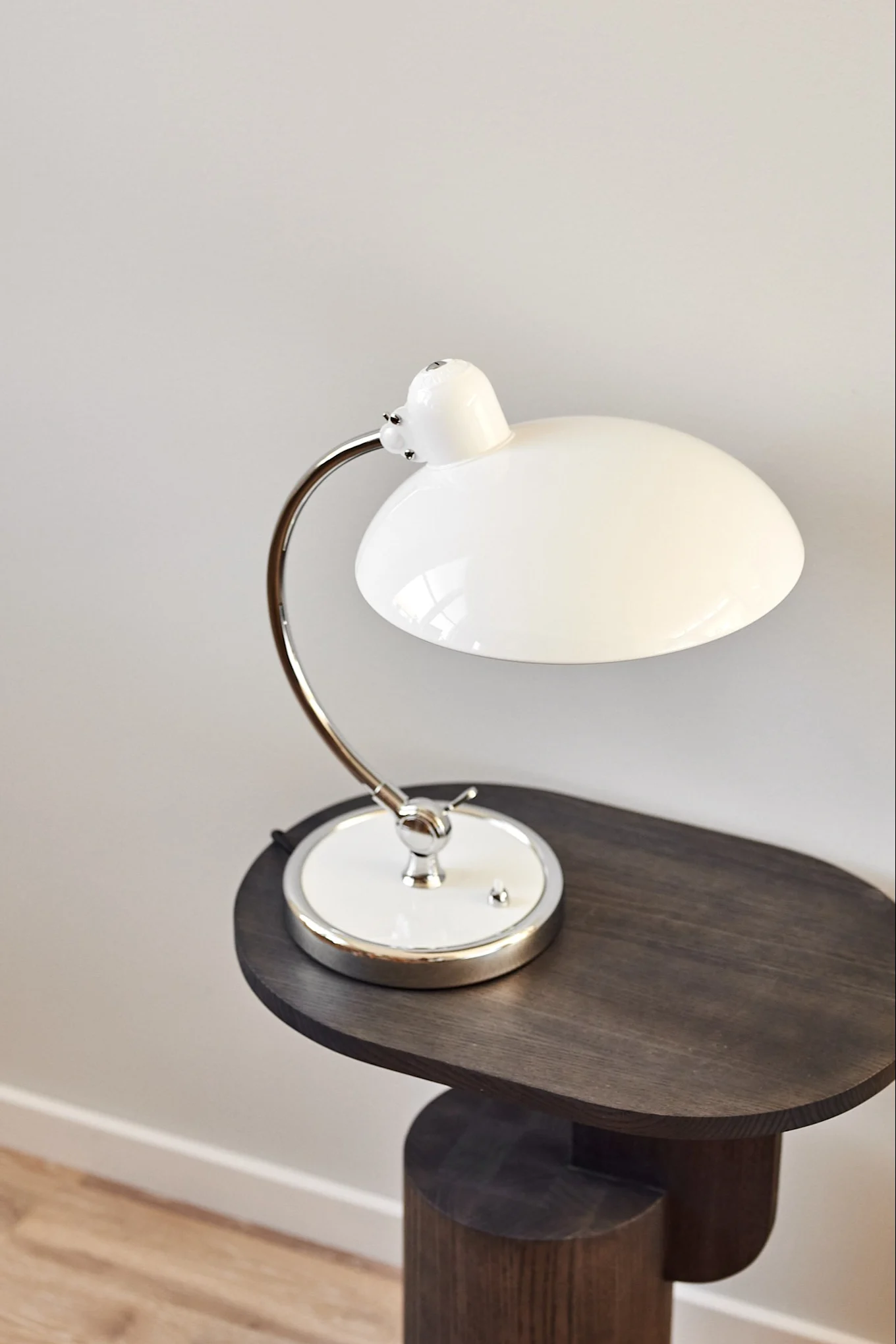 En vit stilren design lampa från Fritz Hansen står på ett mörkt litet träbord.