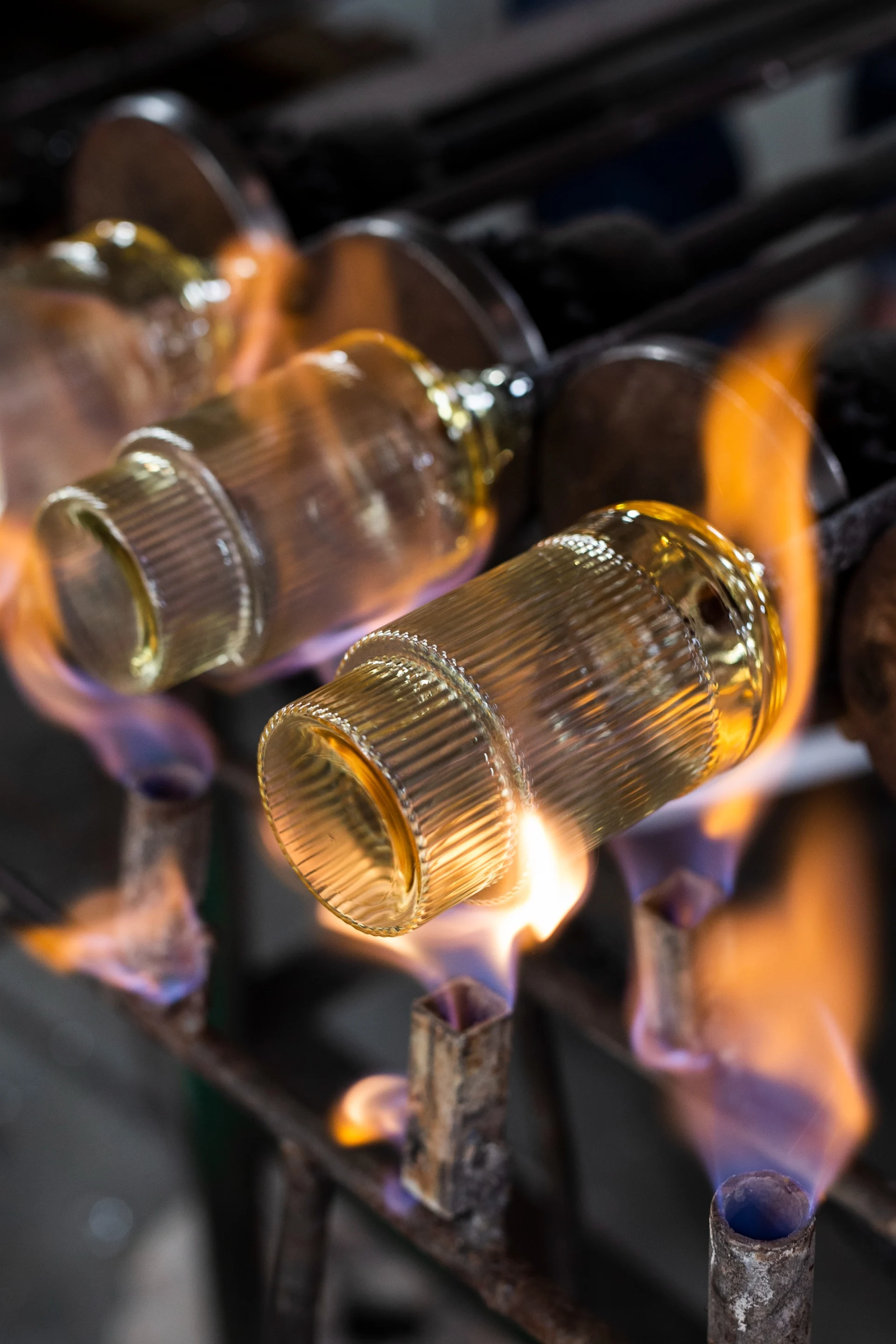 Ribbade cylindriska glasobjekt värms av lågor i en verkstad.