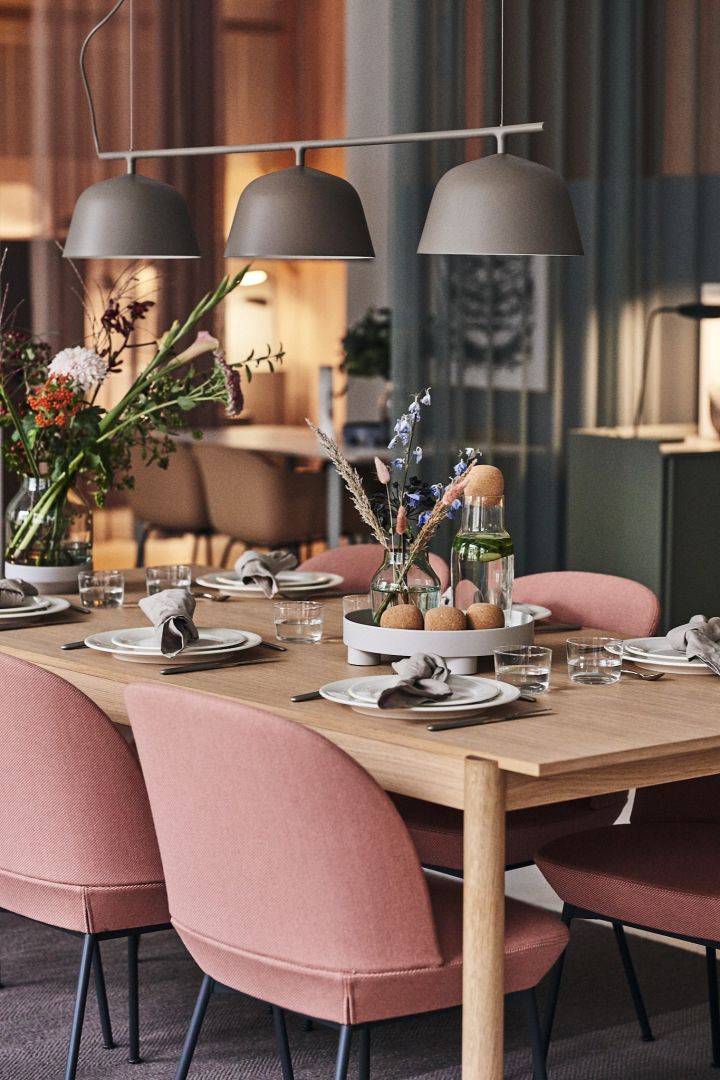 En matplats i rosa och grå toner hos varumärket Muuto med rosa matstolar och en enkel vardagsdukning på vitt porslin.