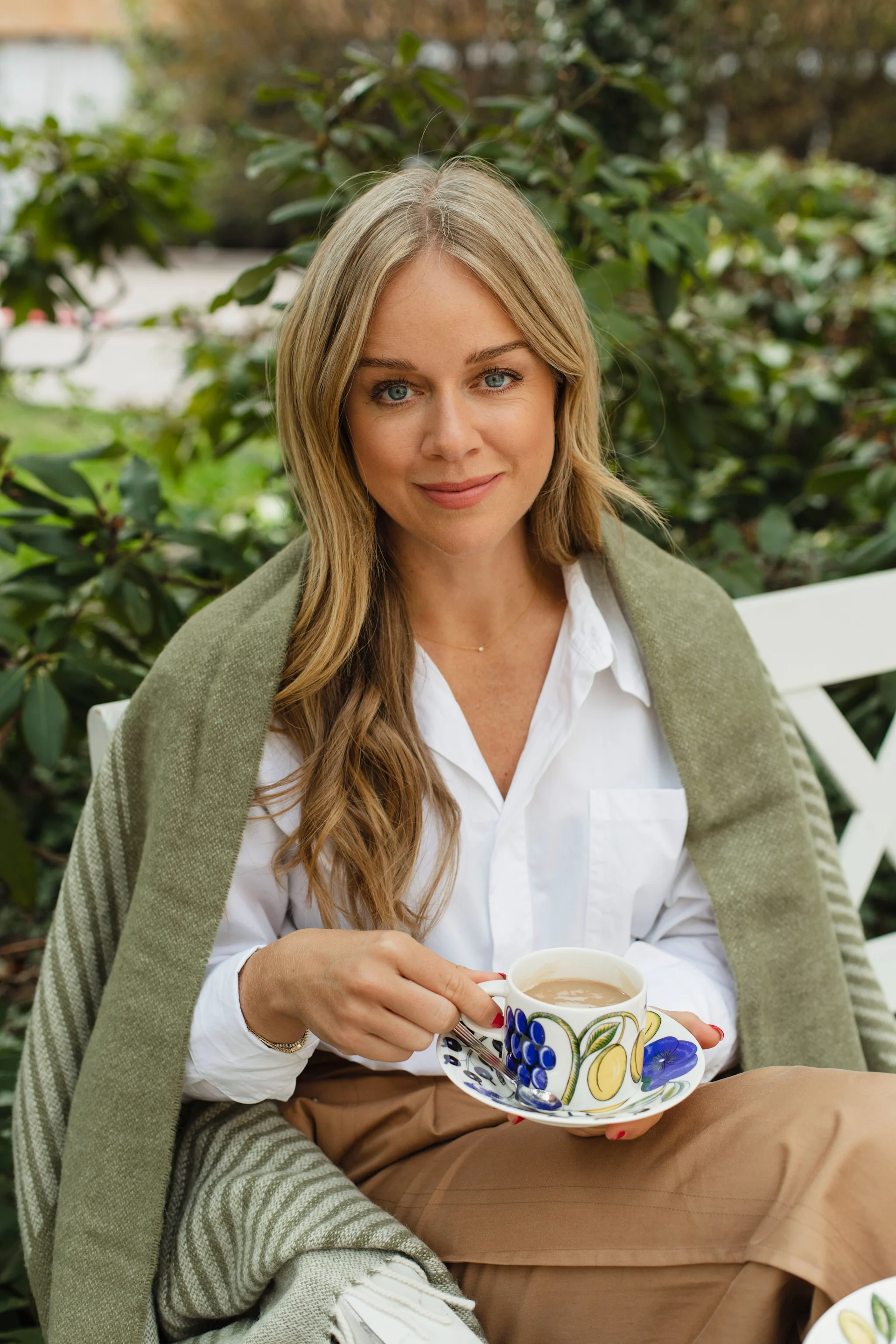 Ebba Kleberg von Sydow håller i den tidlösa designklassikern Paratiisi tekopp med fat från Arabia med Circles ullpläd i grönt från NJRD bakom sig.