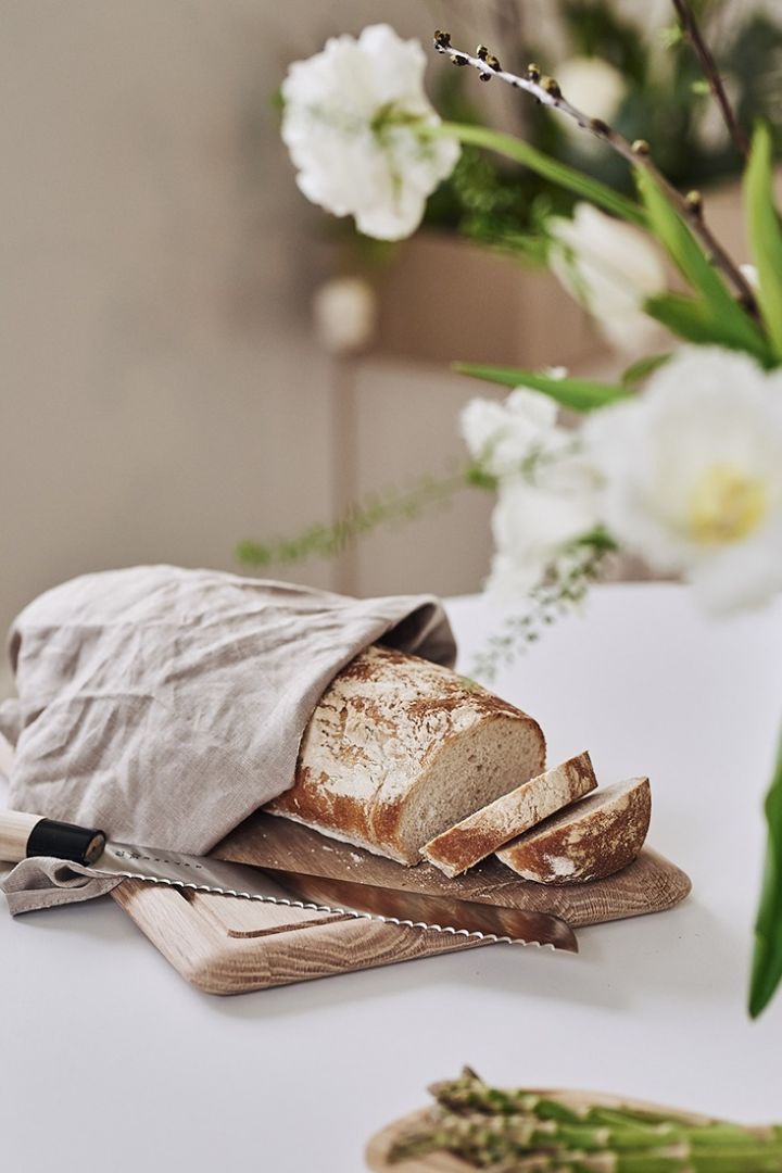 Bröd ligger på skärbräda från Skagerak och täcks med kökshandduk i linne för gästerna att ta för sig av på vårmiddagen. 