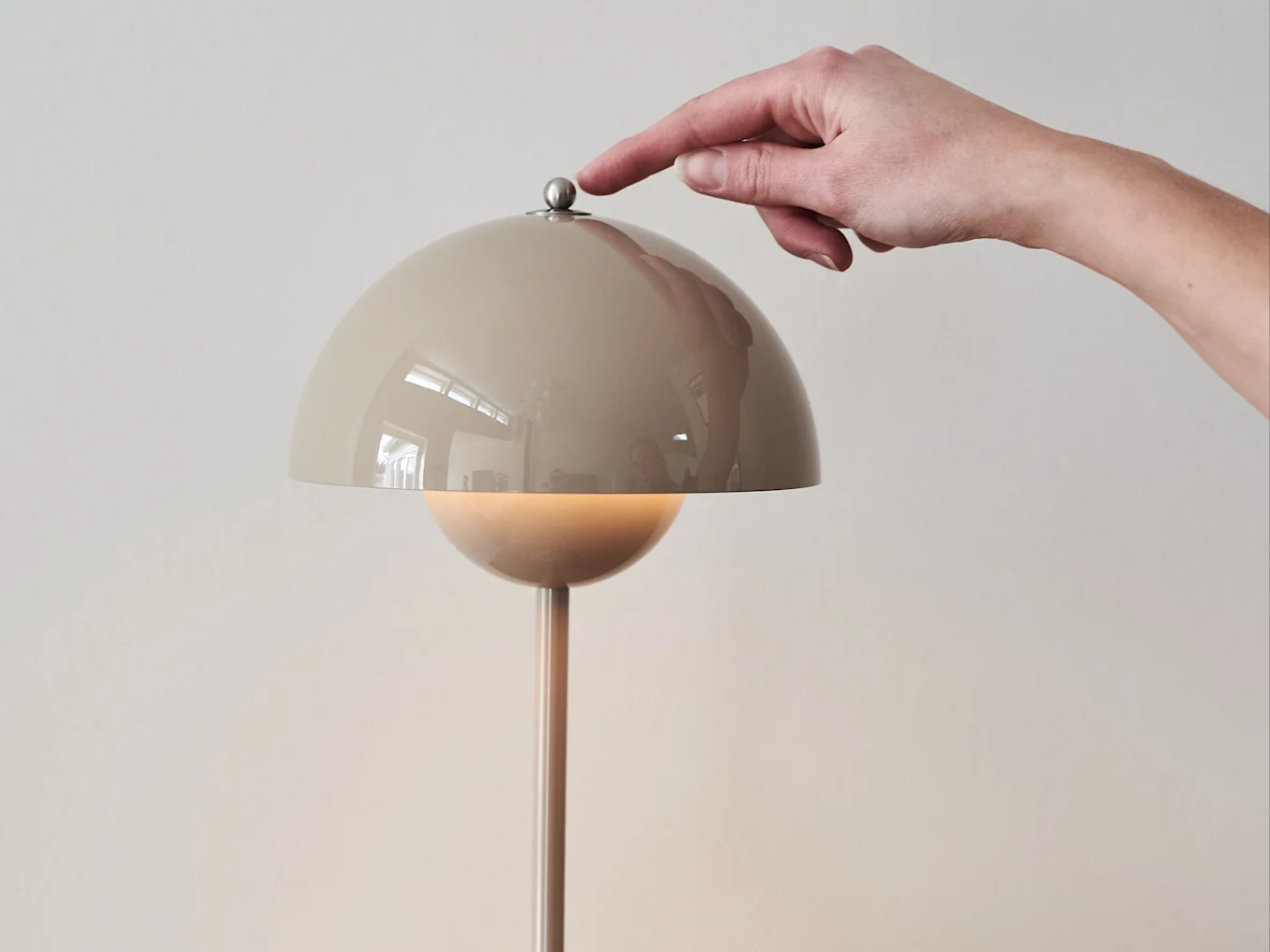 Hand trycker på en metallisk knapp på en beige kupolformad lampa, som avger ett varmt sken.