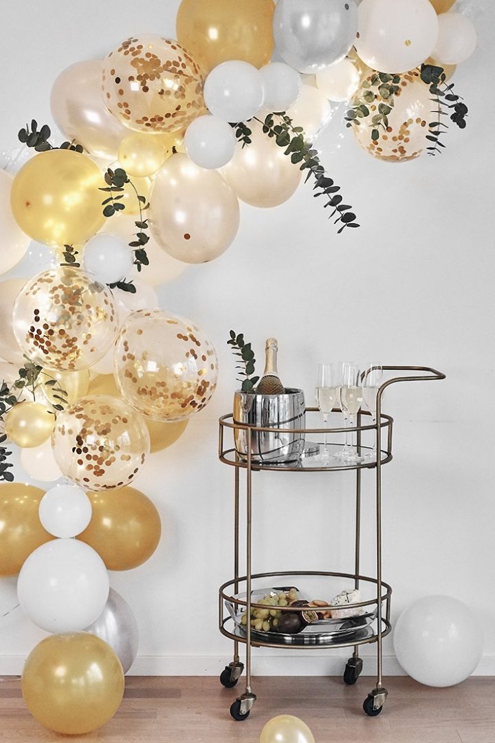 En ballongvägg i guldiga toner ramar in nyårsfestens serveringsvagn. 