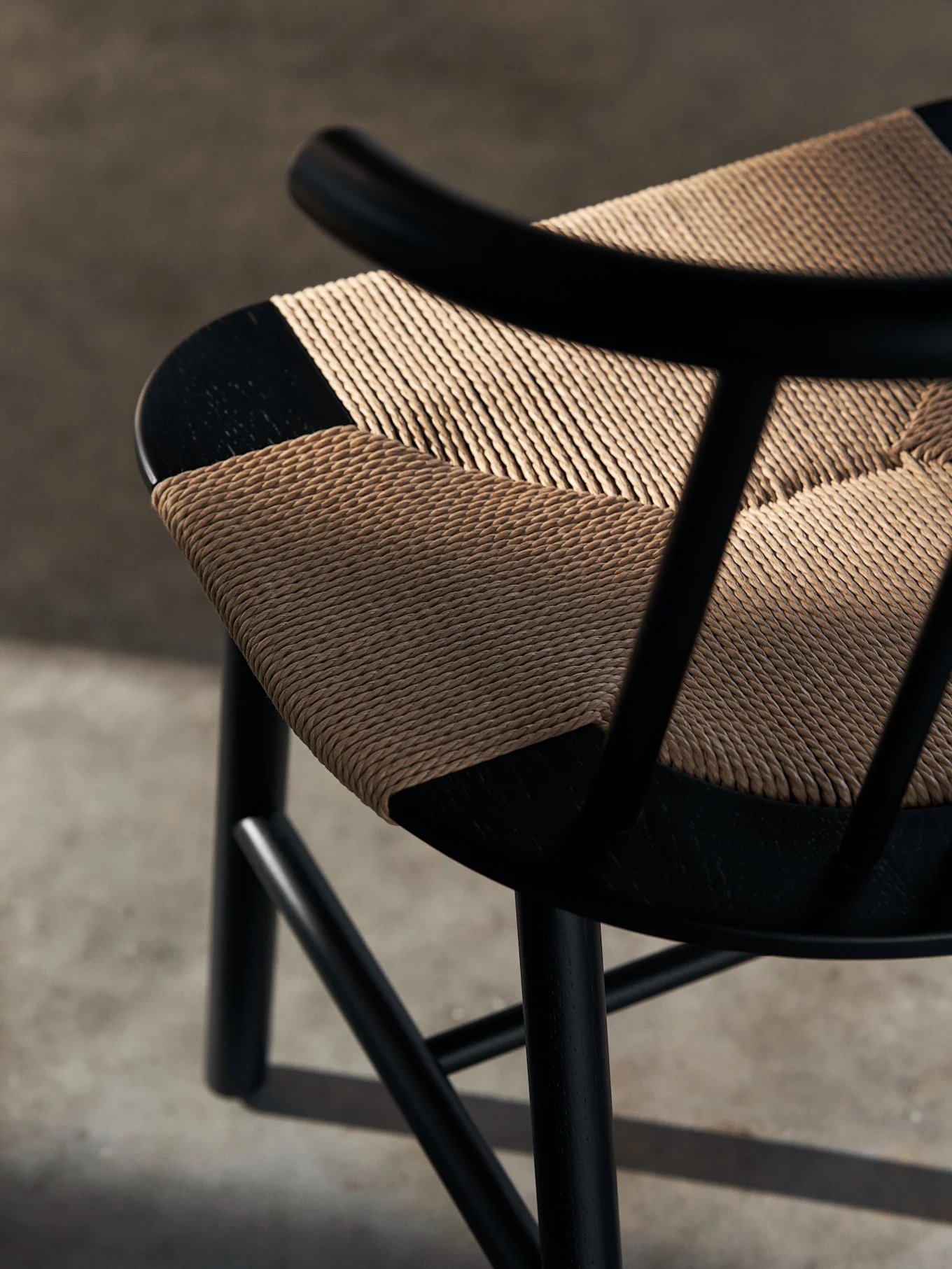 Närbild av en svart trästol med en ljusbrun, diagonalt vävd sits. Skuggor faller över den texturerade sitsen.