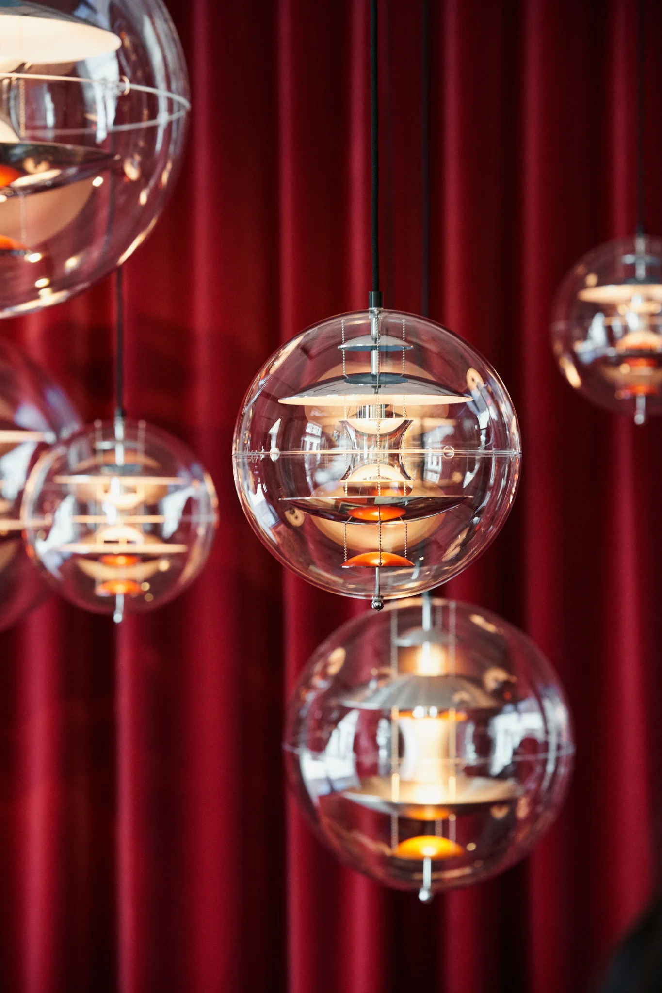 Flera Globe Glass-pendlar från Verpan hänger från taket framför en röd gardin.