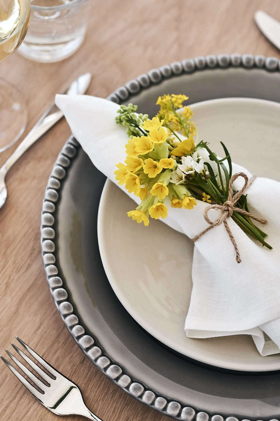 Tallrikskuvert på midsommardukning där servetten lindats in med sju sorters blommor för ett sött och inbjudande uttryck.