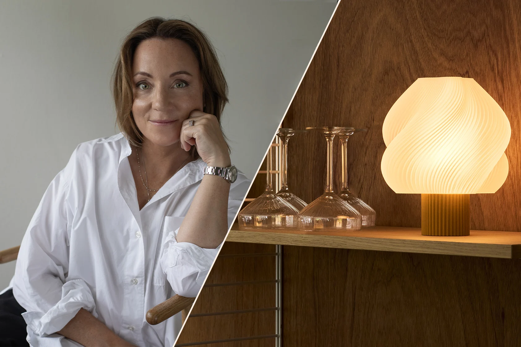 Leende kvinna i vit skjorta, med hakan i handen, bärande en klocka, i en varm, modern interiör med hyllor och en lampa.
