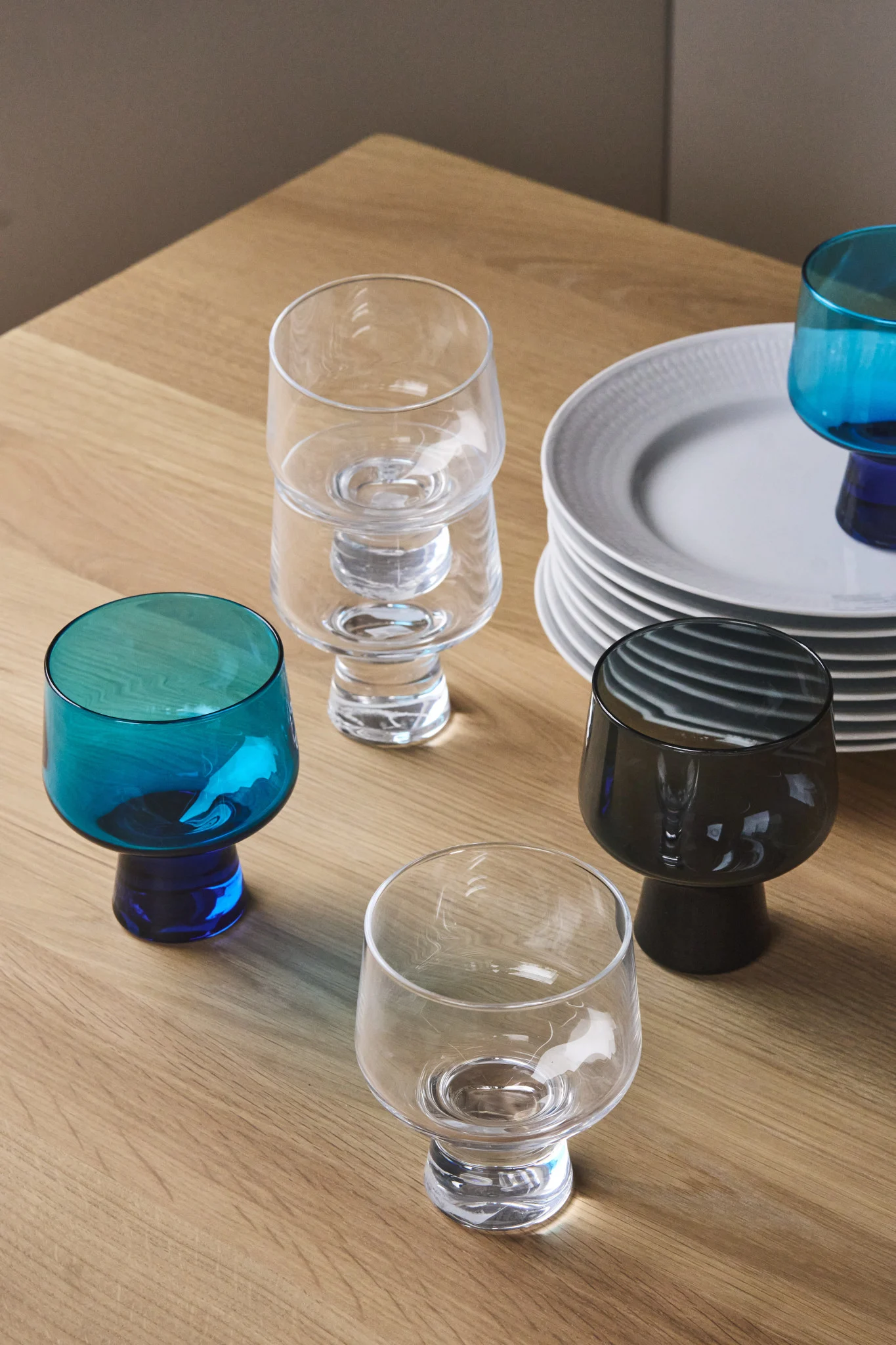 Här ser du en samling glas från Solare-kollektionen från Iittala tillsammans med en hög vita tallrikar. 