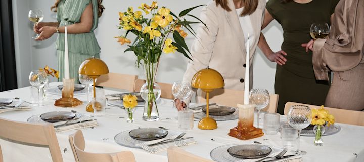 Så här ordnar du en fest med riktig feststämning, här ser du ett dukat bord med gula accenter och gäster som minglar runt bordet. 