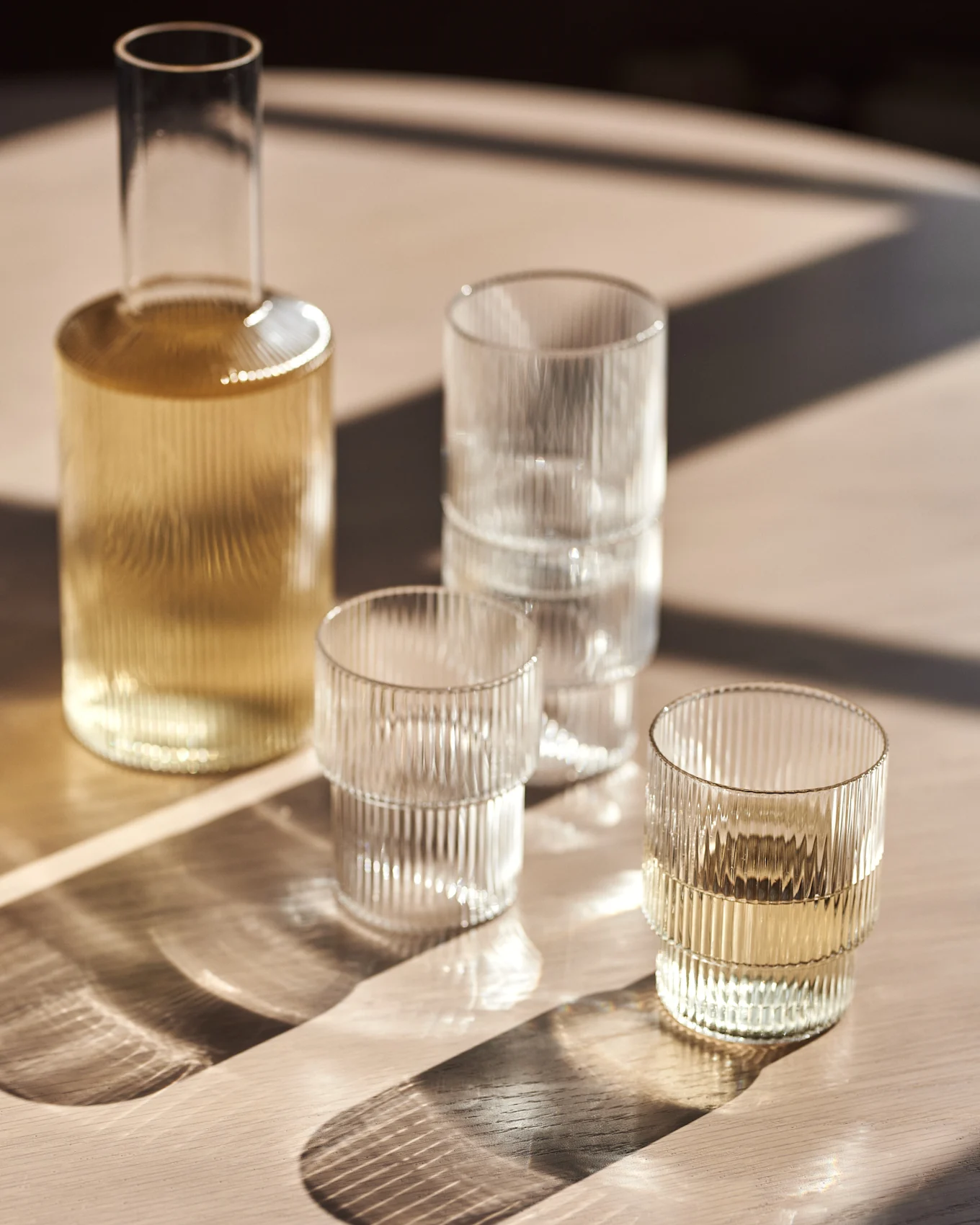 Glaskaraff och räfflade glas på ett träbord med solljus.