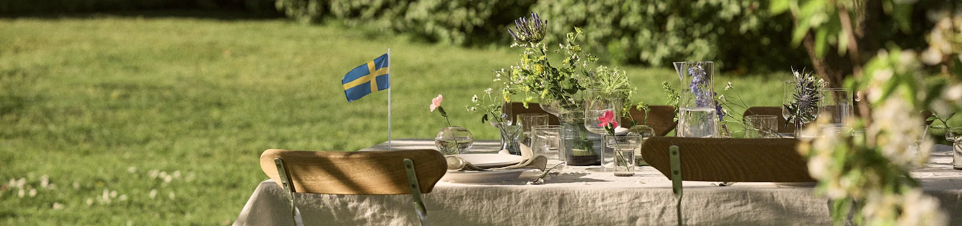 Utedukning med svensk flagga, sommarblommor och glasvaror på dukat bord.