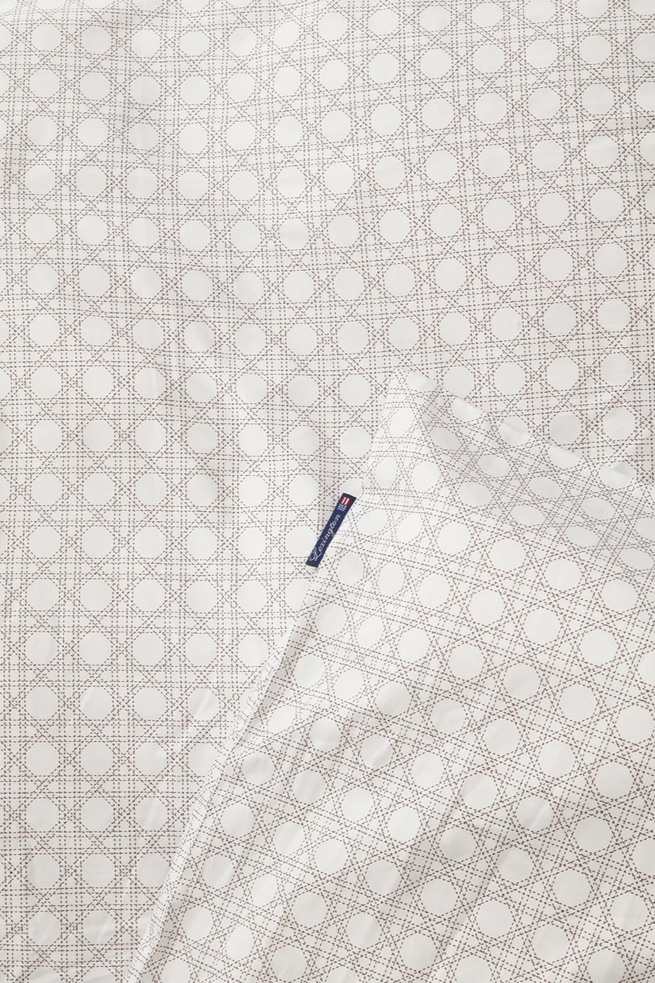 Vitt tyg med ljusbrunt rottingmönster och en blå Lexington-etikett.