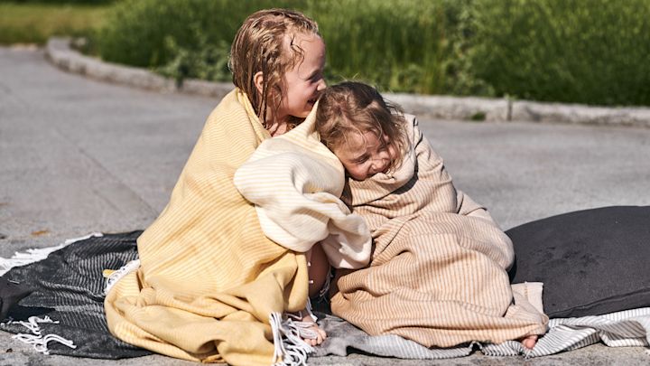 Insvepta i mjuka bomullsplädar från Nordic Nest myser barnen vid poolen efter ett svalkande dopp i poolen. 