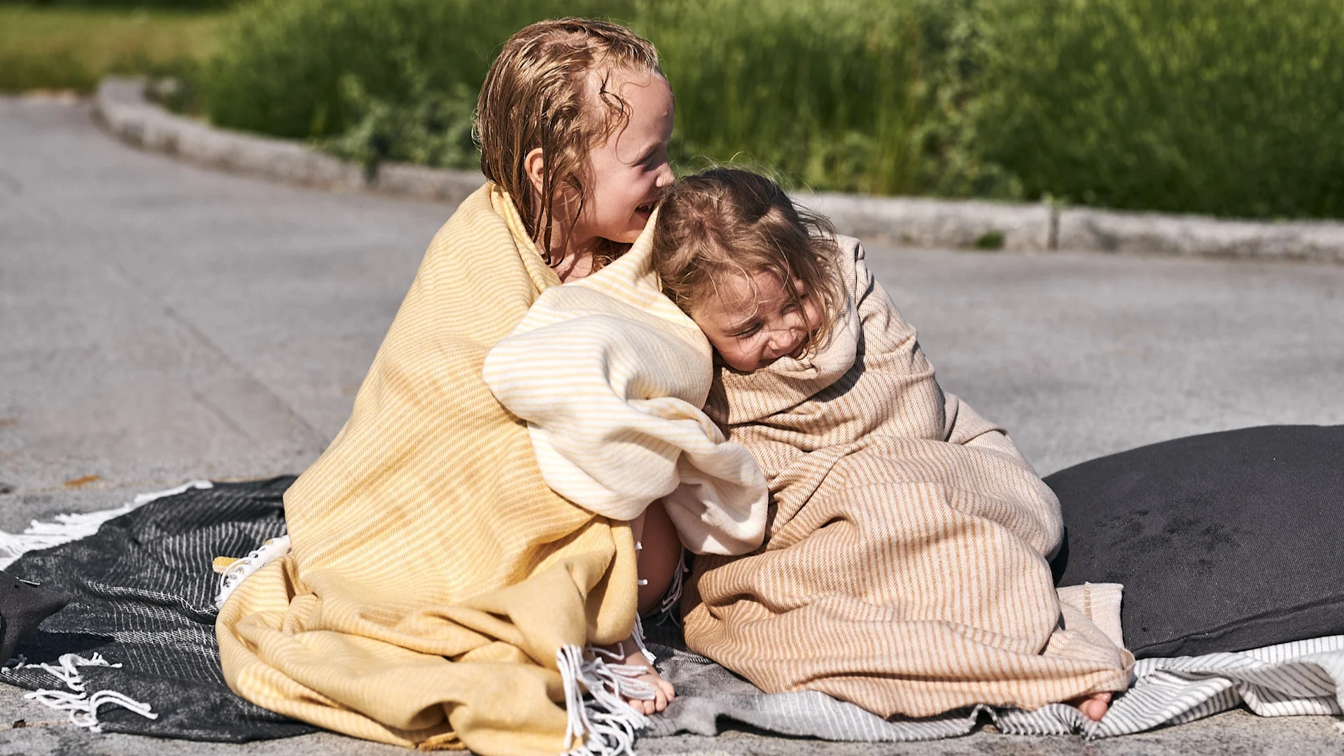 Insvepta i mjuka bomullsplädar från Nordic Nest myser barnen vid poolen efter ett svalkande dopp i poolen.