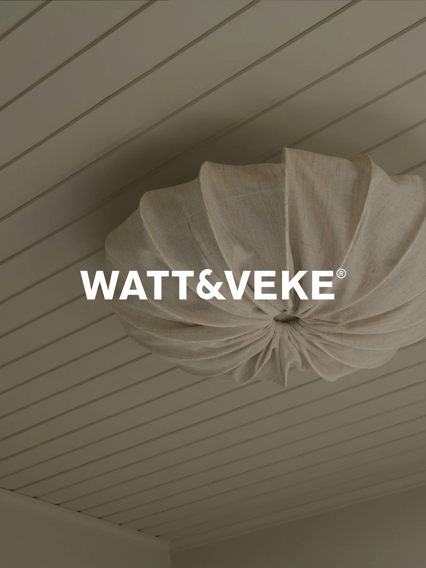 WATT&VEKE®-logotyp över en plisserad taklampa i naturtyg på ett ljust träpanelstak.