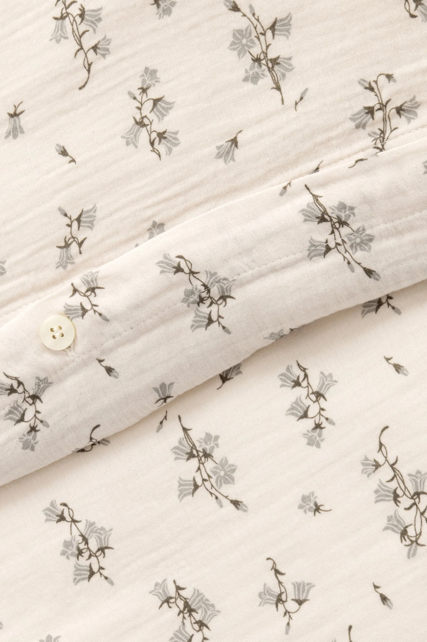 Närbild på krämfärgat tyg med grått klockblommönster och en vit knapp.