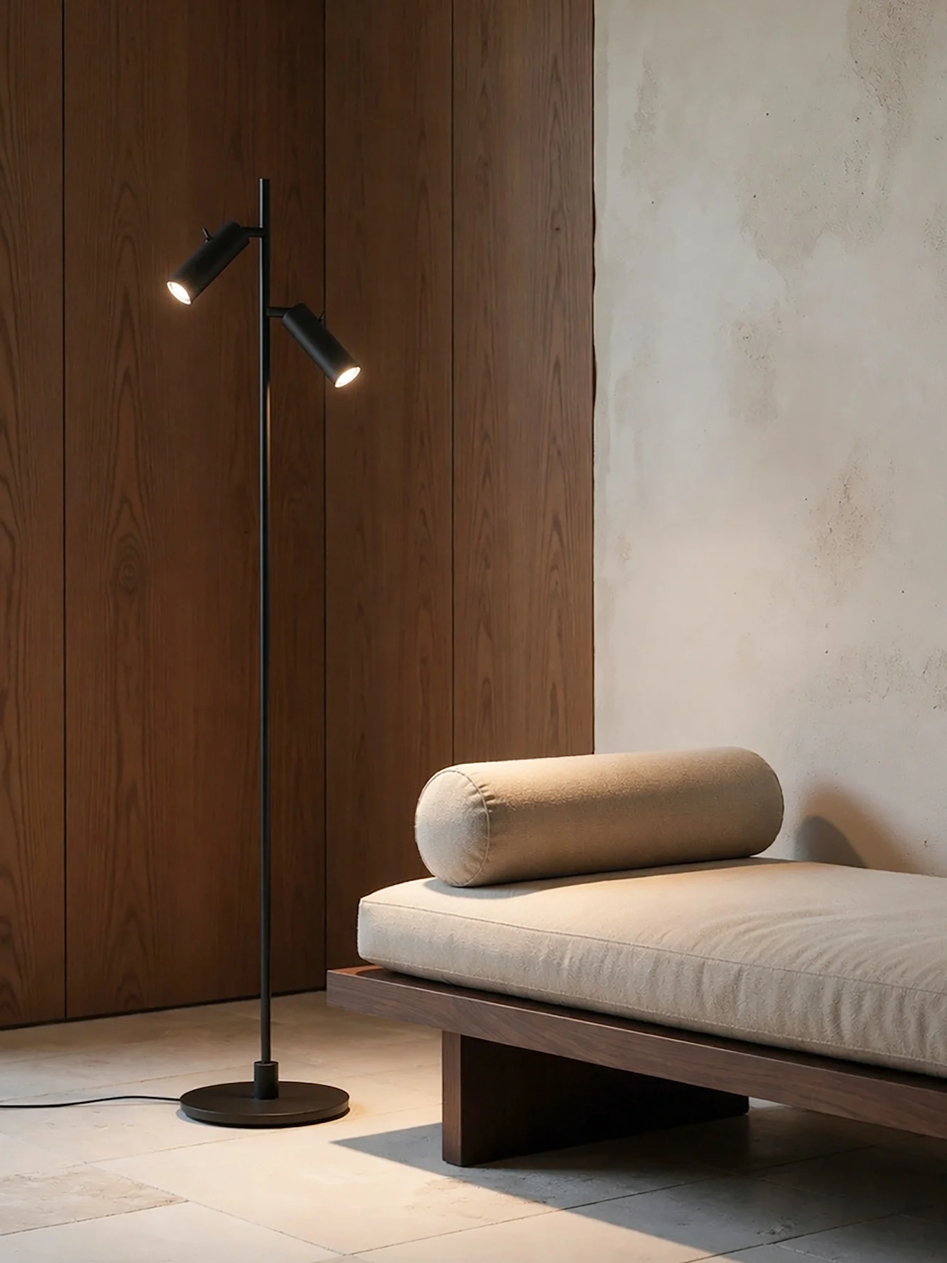 Ett modernt rum med en svart golvlampa med två ljus bredvid en trädaybed med en ljusbeige dyna och en bolsterkudde.
