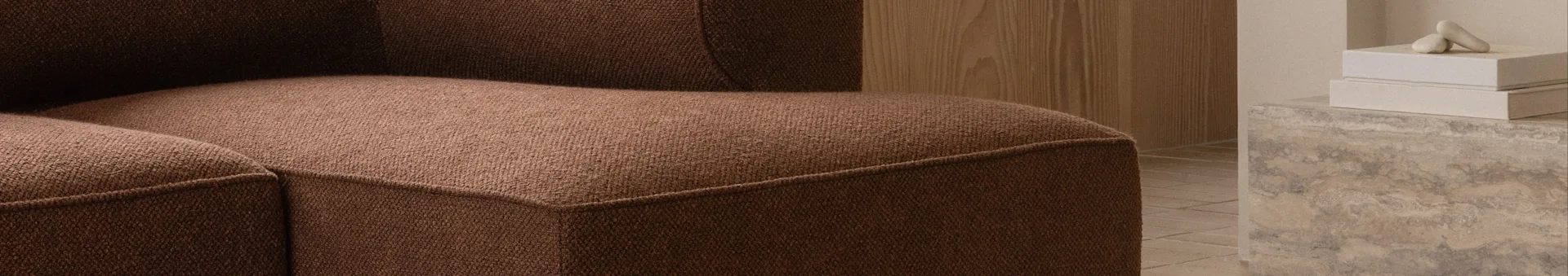 Närbild av en brun texturerad soffa, med en trävägg och dekorativa föremål på en betongyta i bakgrunden.
