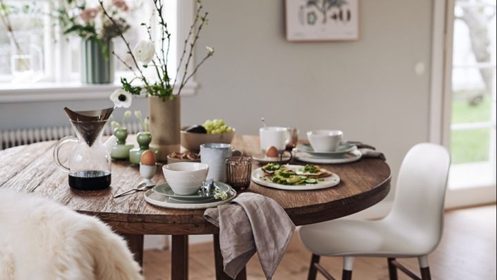 En vårlig frukostdukning i gröna toner med vårblommor, grönt porslin och vita matstolar i en matplats i skandinavisk stil.
