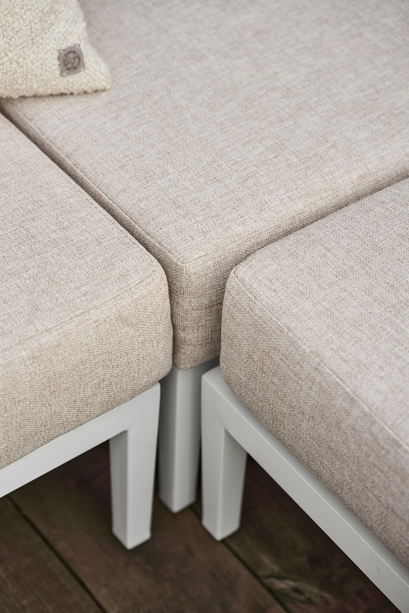 Närbild på ljusbeige texturerade utomhussoffdynor på en vit ram, med en liten prydnadskudde. Inspiration till din balkong 2026.