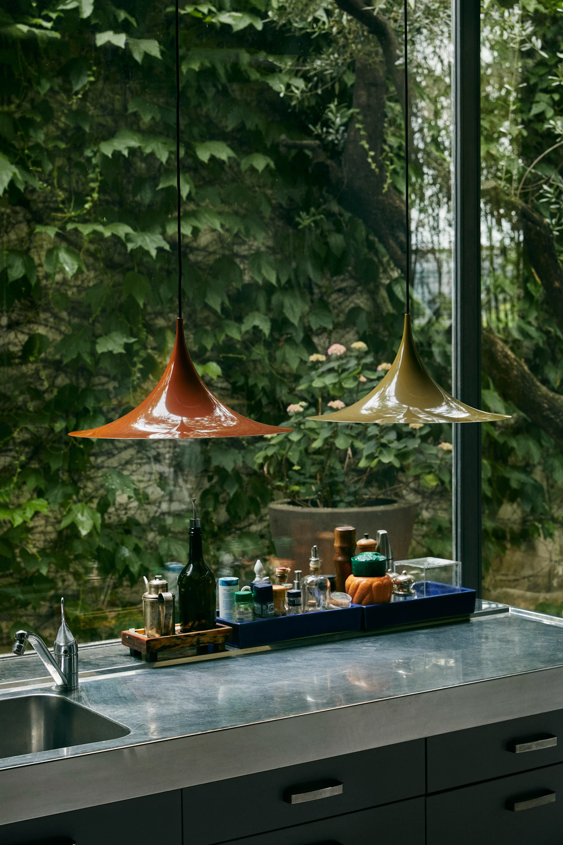 Två Semi pendel taklampor från Gubi i orange och grönt hänger i ett kök. Lampan tillhör en klassisk designlampa. 