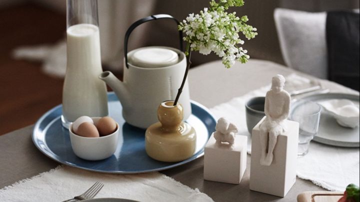En frukostdukning med ett stilleben på bordet med drömska Kähler skulpturer och gul Marimekko vas på en blå bricka.