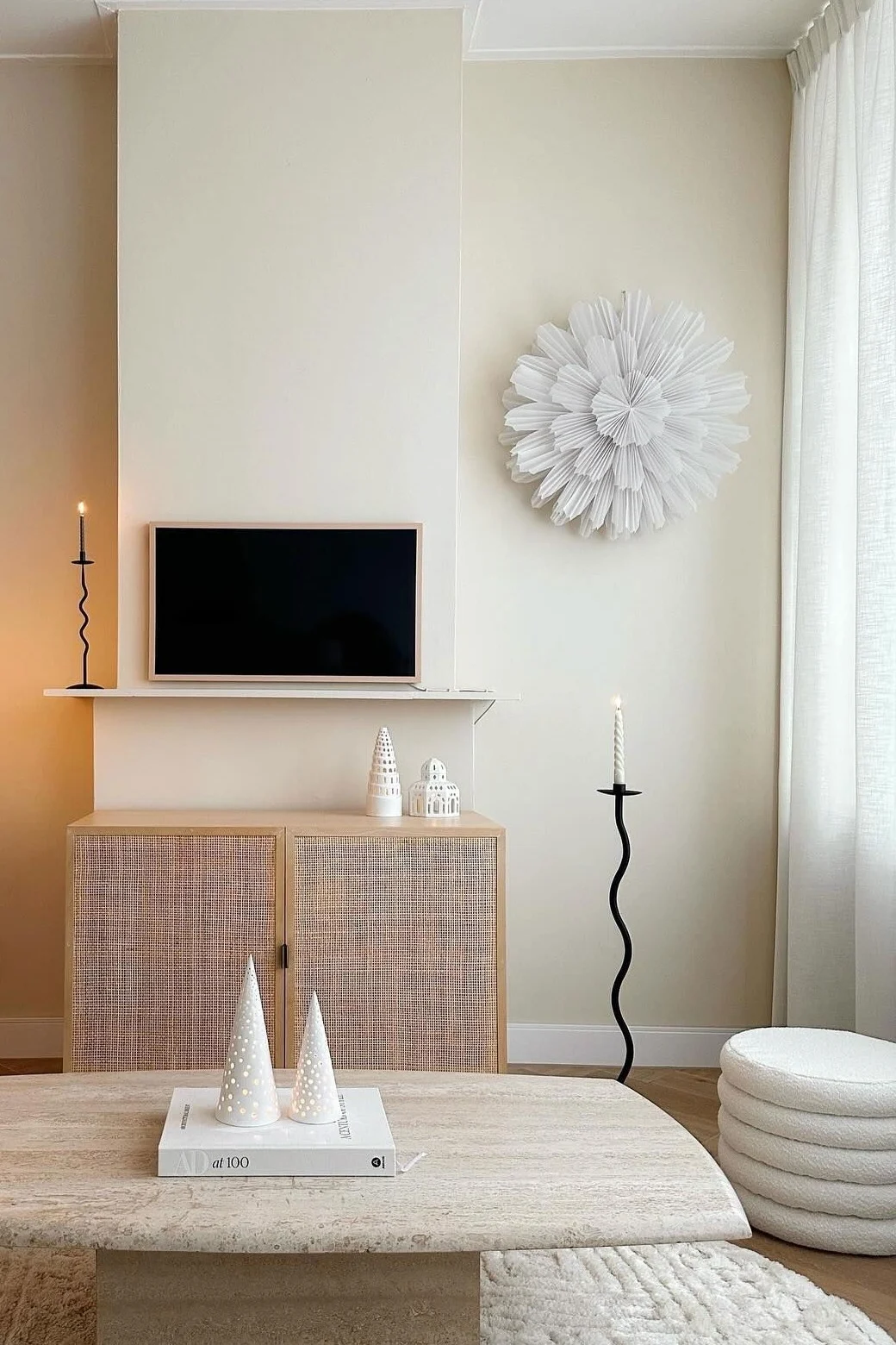Neutralt vardagsrum med texturerad matta, travertin soffbord, rottingskåp, TV, golvlampa och plisserad väggdekor.