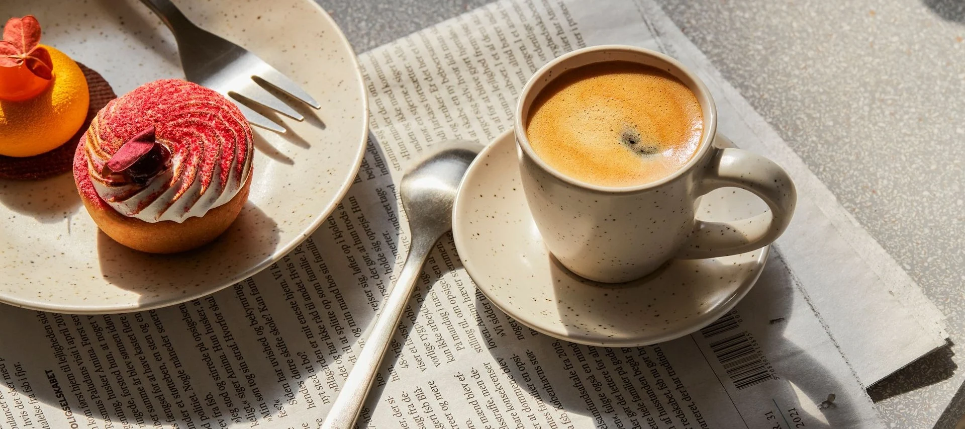 Kaffekopp och två bakverk, en röd tårta och en orange, på en tidning.