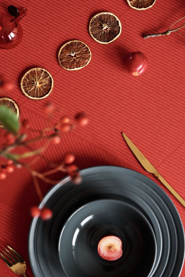 Återskapa en traditionell röd juldukning 2021 från NJRD - här ser du Lines mörkgrå tallrik och skål i mörkgrå tillsammans med Tvis bestick i guld från Broste Copenhagen.