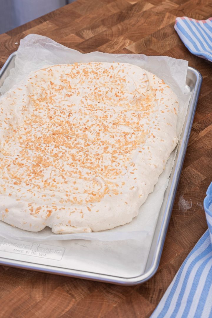 Baka en god marängtårta med hjälp av Baka med Fridas enkla påskrecept på en bakplåt från Nordic Ware. Strö över kokos på din marängbotten som ger extra krisp.