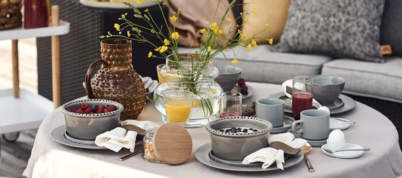 En lyxig och mysig hotellfrukost hemma står uppdukad på terrassen med smoothie bowls, kaffe och juicer.