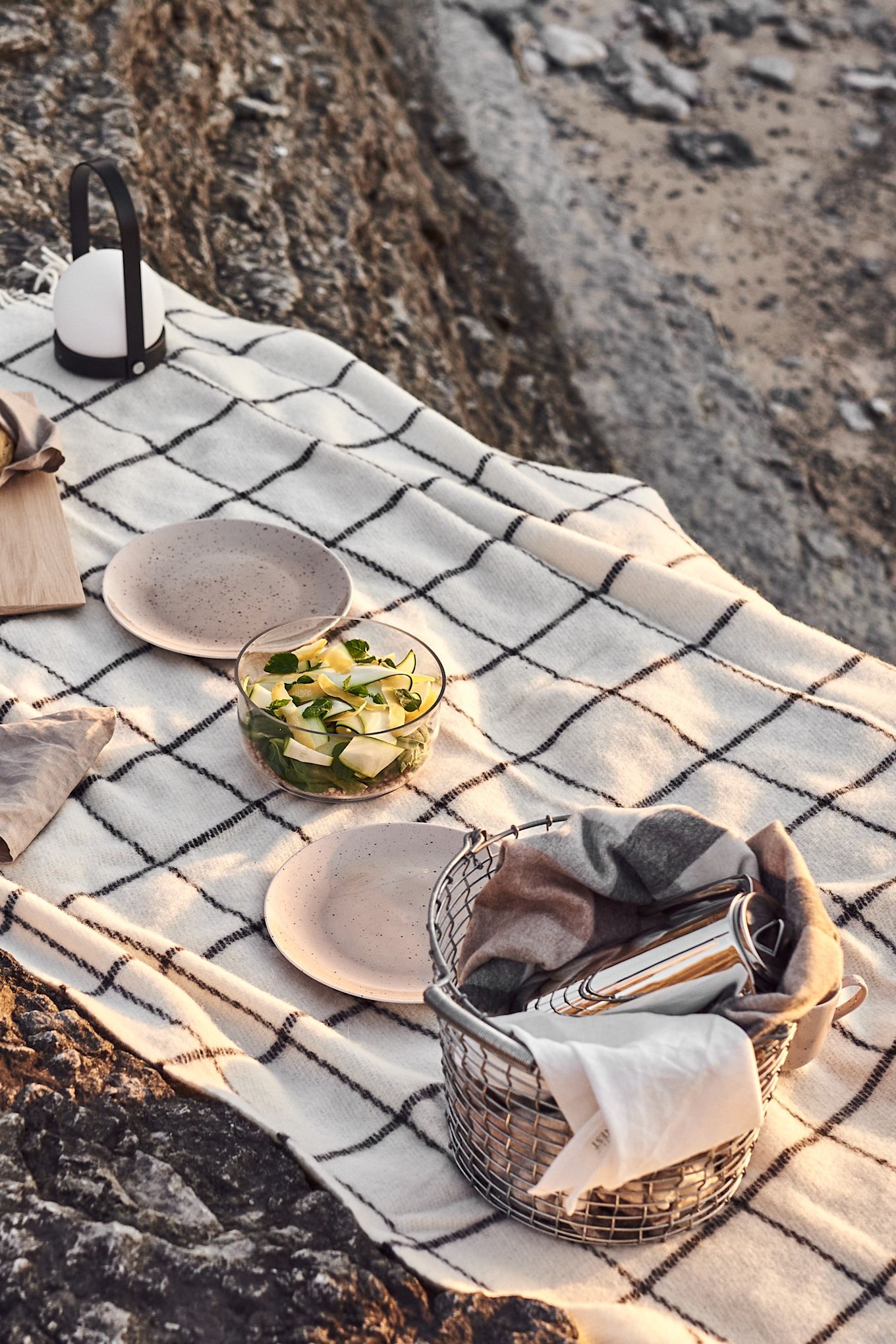 Picknick på rauckar med shackrutig pläd, portabel belysning. porslin och en sallad. 