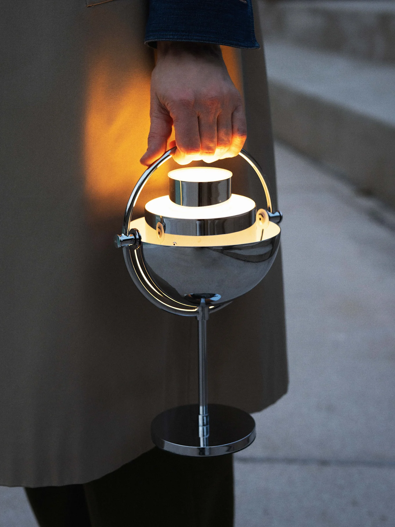 Hand håller en glödande, modern kromad portabel lampa.