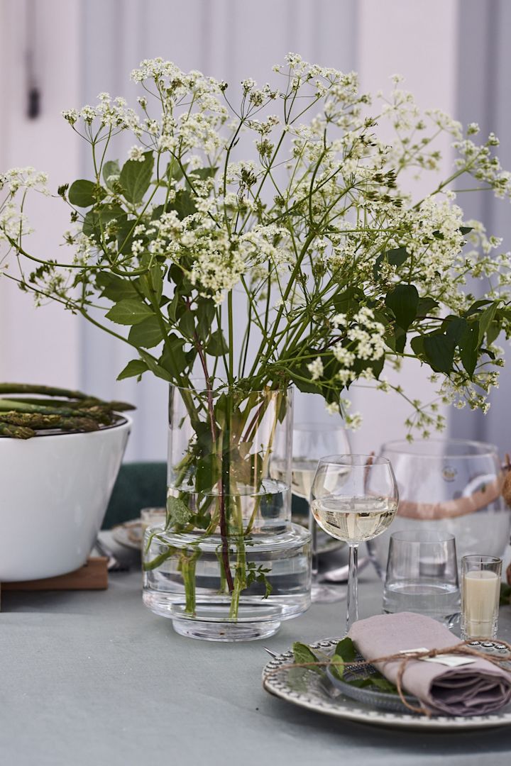Ett fång med trädgårdsblommor huserar i hög vas i klarglas från Ro Collection på trädgårdsfestens dukning. 