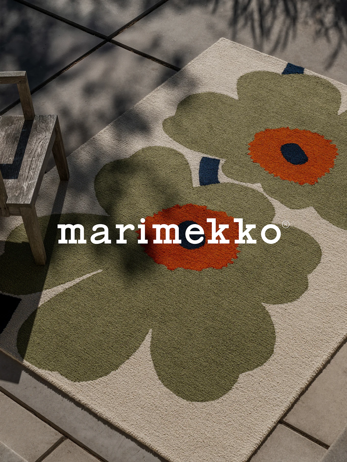 Marimekko-matta med stort grönt och orange blommönster på en uteplats med en trästol.