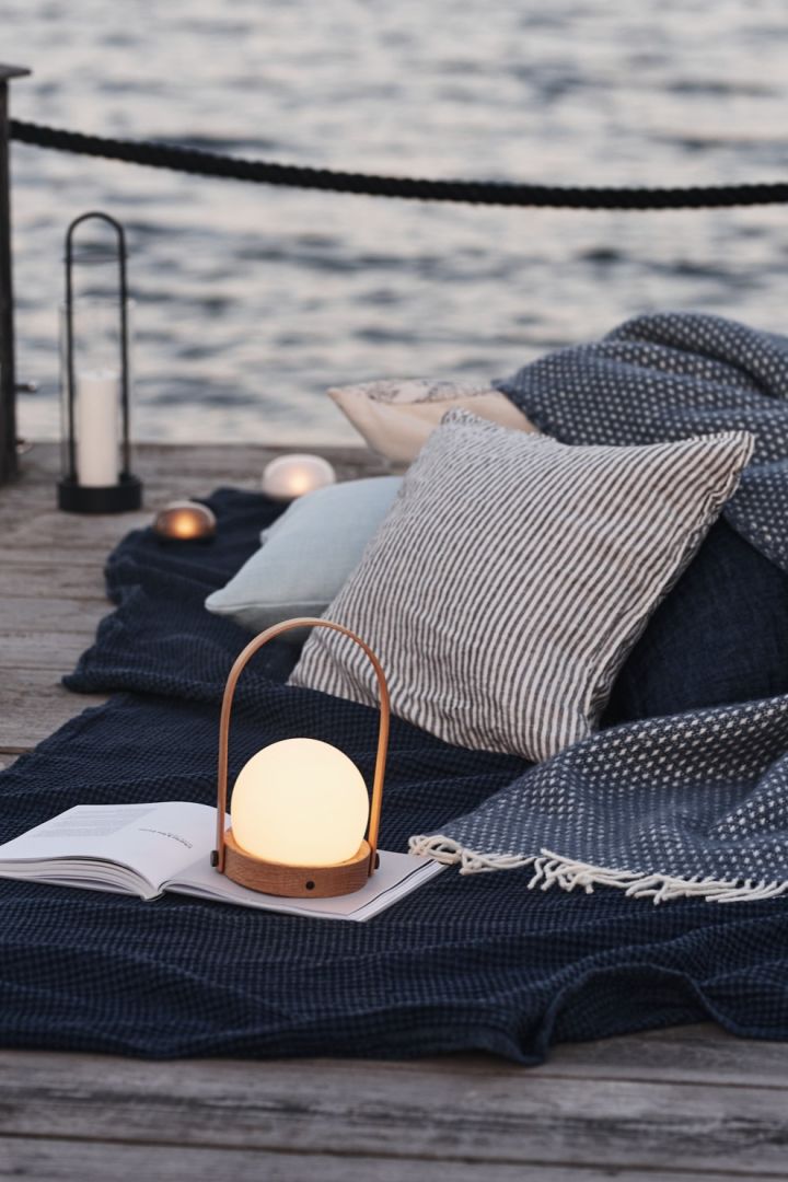 En mysig picknick på bryggan blir perfekt när du tar med din uppladdningsbara lampa - här Carrie i ek från Audo Copenhagen. 