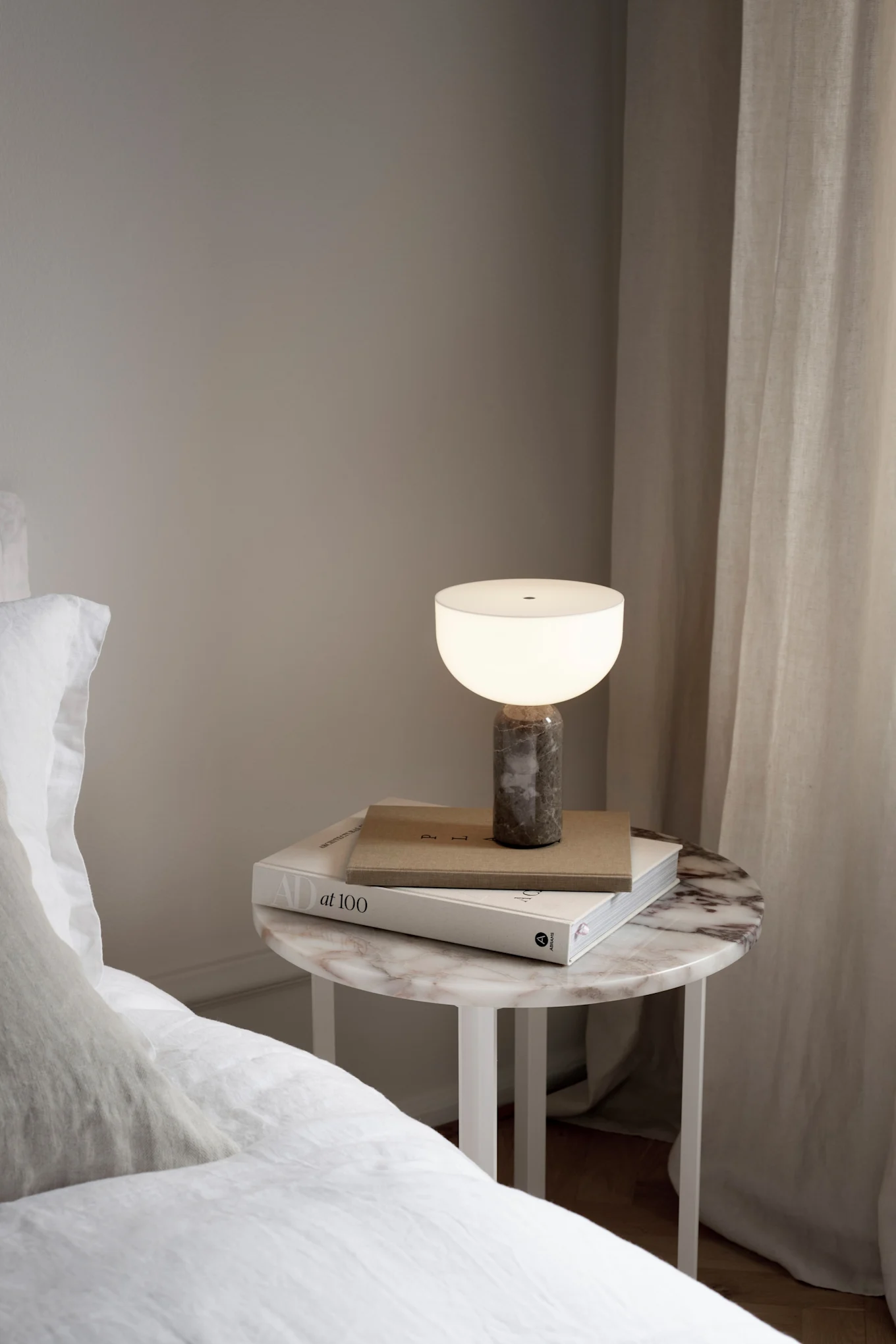 Kizu uppladdningsbara lampa står på ett nattduksbord brevid en säng.