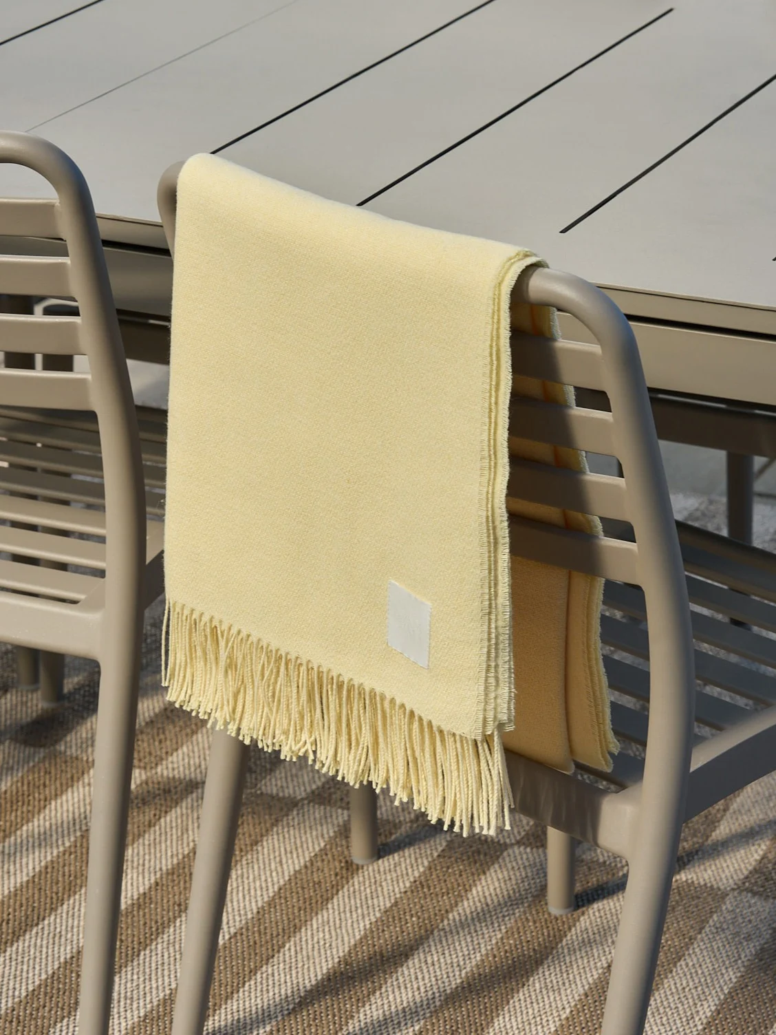 Ljusgul filt med fransar draperad över en beige utomhusstol.