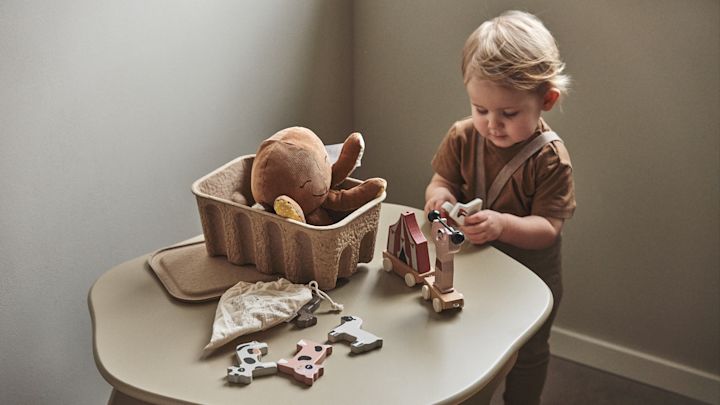 I ett barnrum är det viktigt att både det kreativa och praktiska ryms. Här litet barn som leker med klossar på Slope barnbord i beige, från Ferm Living.