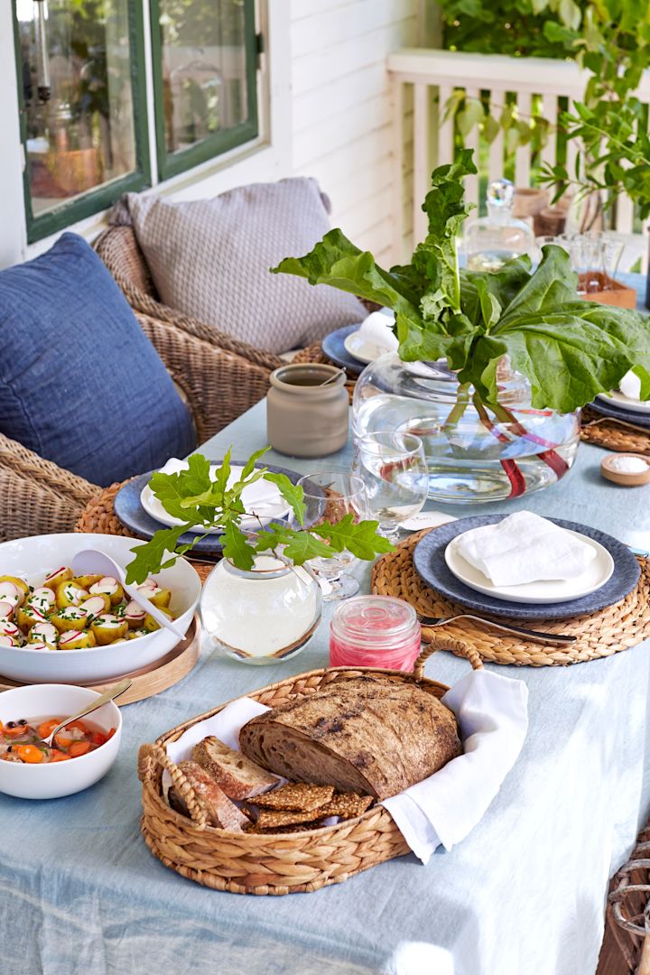 Duka till midsommar i en modernt rustik stil med rustikt porslin, flätad brödkorg och rabarber i vas. 