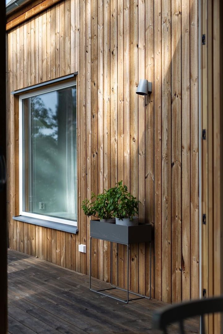 Här ser du den svarta växtlådan i metall från Ferm Living stå på terrassen till ett svenskt trähus.